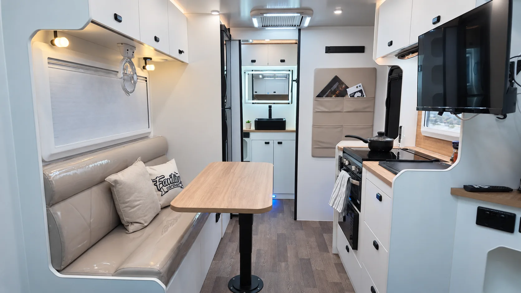 Skyline caravan interior with a cushioned dinette, timber table, kitchen bench and overhead TV